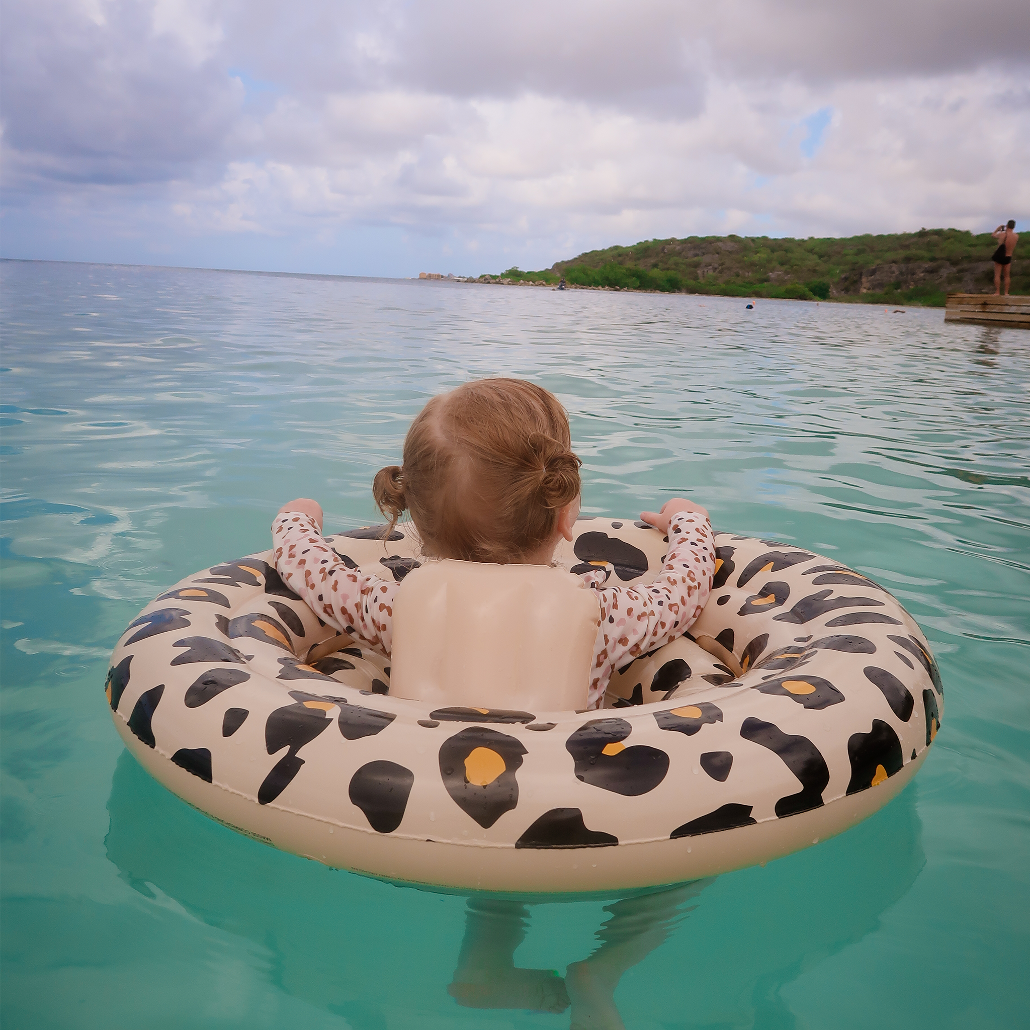 Kindje op vakantie in de zee in haar beige panterprint babyfloat van swim essentials